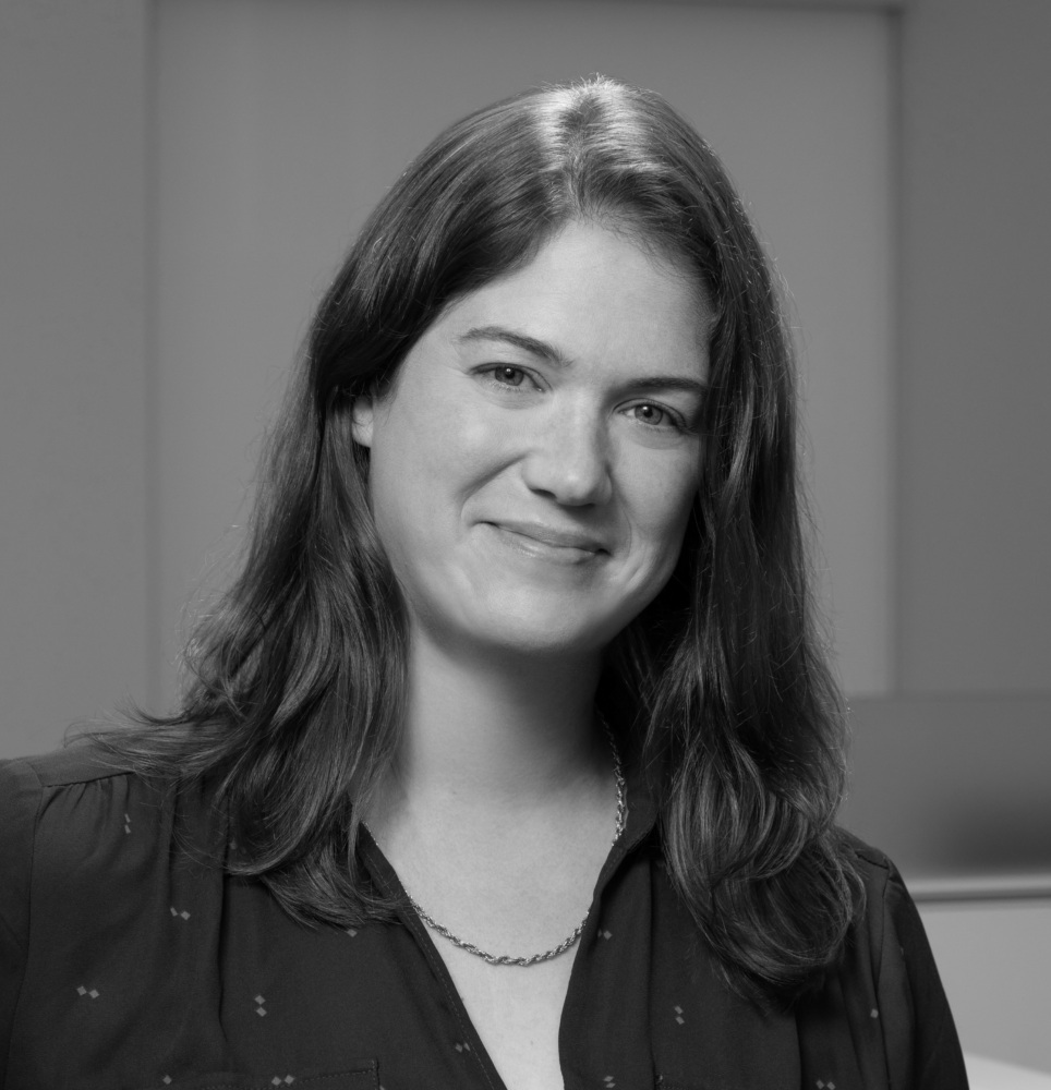 Black and white photograph of a woman looking into the camera, smiling, and wearing a dark-colored shirt and necklace.